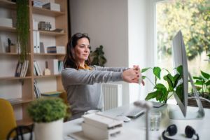 Attractive businesswoman sitting indoors in office, stretching.